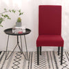 Funda de silla roja de tamaño universal en un entorno moderno con una mesa redonda negra y una alfombra estampada, disponible en blueemoonco.com, especialistas en fundas de sofá y silla.