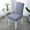 Funda para silla de color gris claro, elástica y texturizada, en un ambiente minimalista con mesa blanca y decoración sutil. Ideal para renovar el mobiliario de casa y disponible en blueemoonco.com.