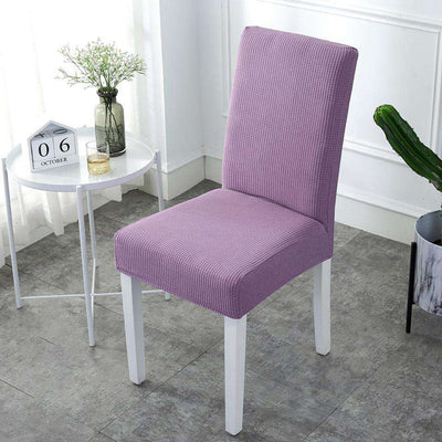 Funda para silla en color violeta texturizado, ajustable y elegante, mostrada en un entorno luminoso con una mesa blanca y decoración minimalista. Ideal para decorar y proteger sillas en hogares y oficinas. Disponible en blueemoonco.com.