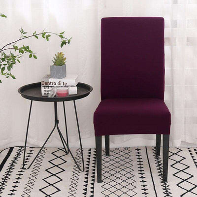 Fundas universales para sillas en color morado, estilo moderno con mesa auxiliar negra y alfombra geométrica en un ambiente luminoso con cortinas transparentes.