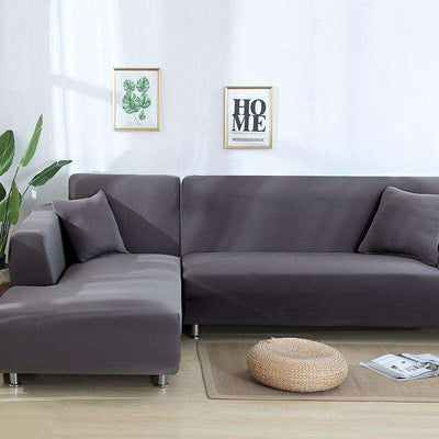 Funda de sofá elástica en color gris, estilo moderno, adecuada para un salón contemporáneo con decoración minimalista. Incluye dos cuadros decorativos con motivos de plantas y la palabra HOME en la pared blanca.
