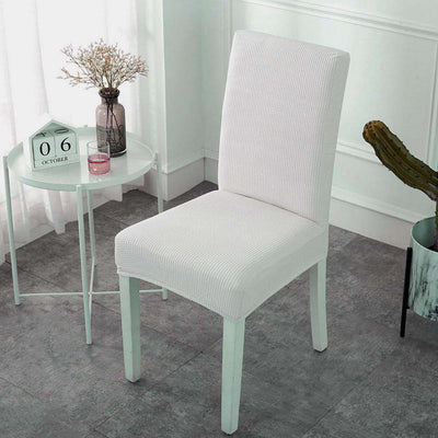 Fundas para sillas color crema en tela texturizada, presentadas en un entorno elegante con mesa blanca y decoración minimalista, perfectas para modernizar y proteger el mobiliario del hogar, disponible en blueemoonco.com.