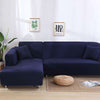 Funda elástica de sofá en color azul marino, estilo moderno con cojines a juego, en un salón decorado con cuadros minimalistas y plantas verdes.