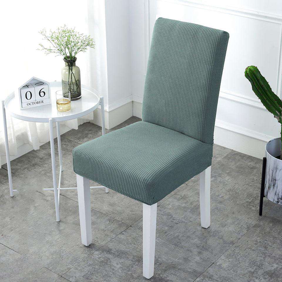 Fundas elásticas para sillas en color verde, perfectamente ajustadas a una silla de patas blancas en un entorno luminoso con una pequeña mesa blanca, un jarrón con flores y una decoración minimalista. Ideal para renovar el estilo de tu comedor con blueemoonco.com