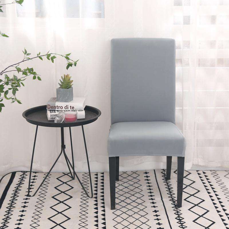 Funda de silla gris claro de blueemoonco.com en un entorno moderno con mesa auxiliar y decoración minimalista.