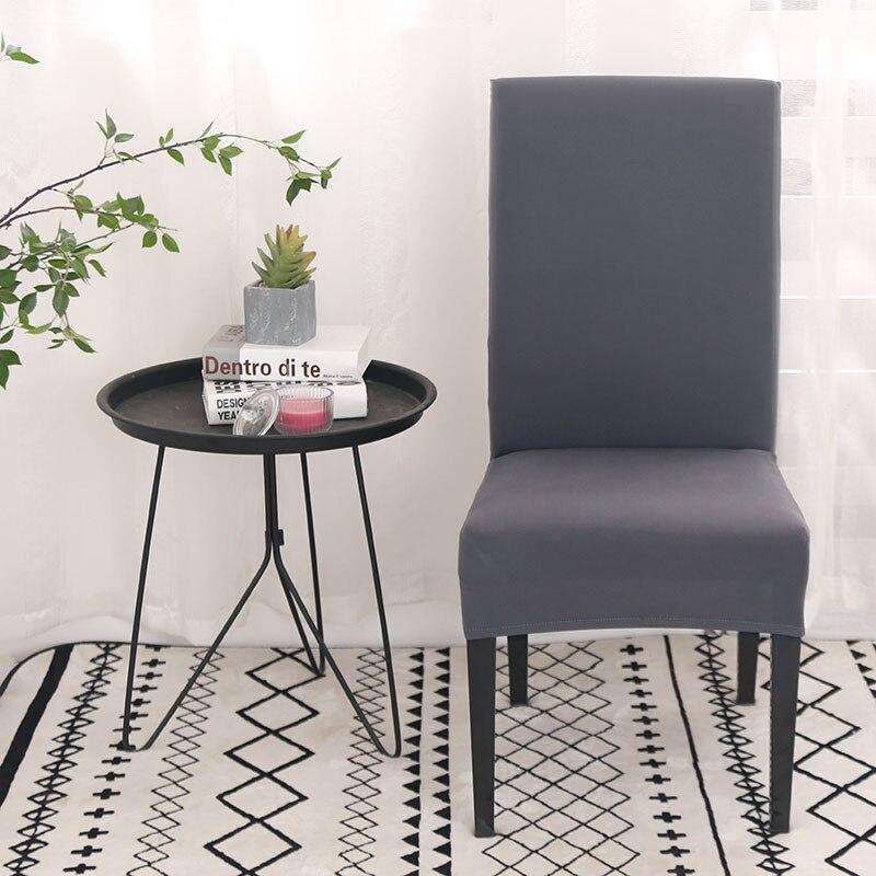 Protector de silla de tela gris sobre fondo blanco con mesa auxiliar negra y planta decorativa, en un interior moderno con alfombra geométrica. Ideal para decoración del hogar en blueemoonco.com.